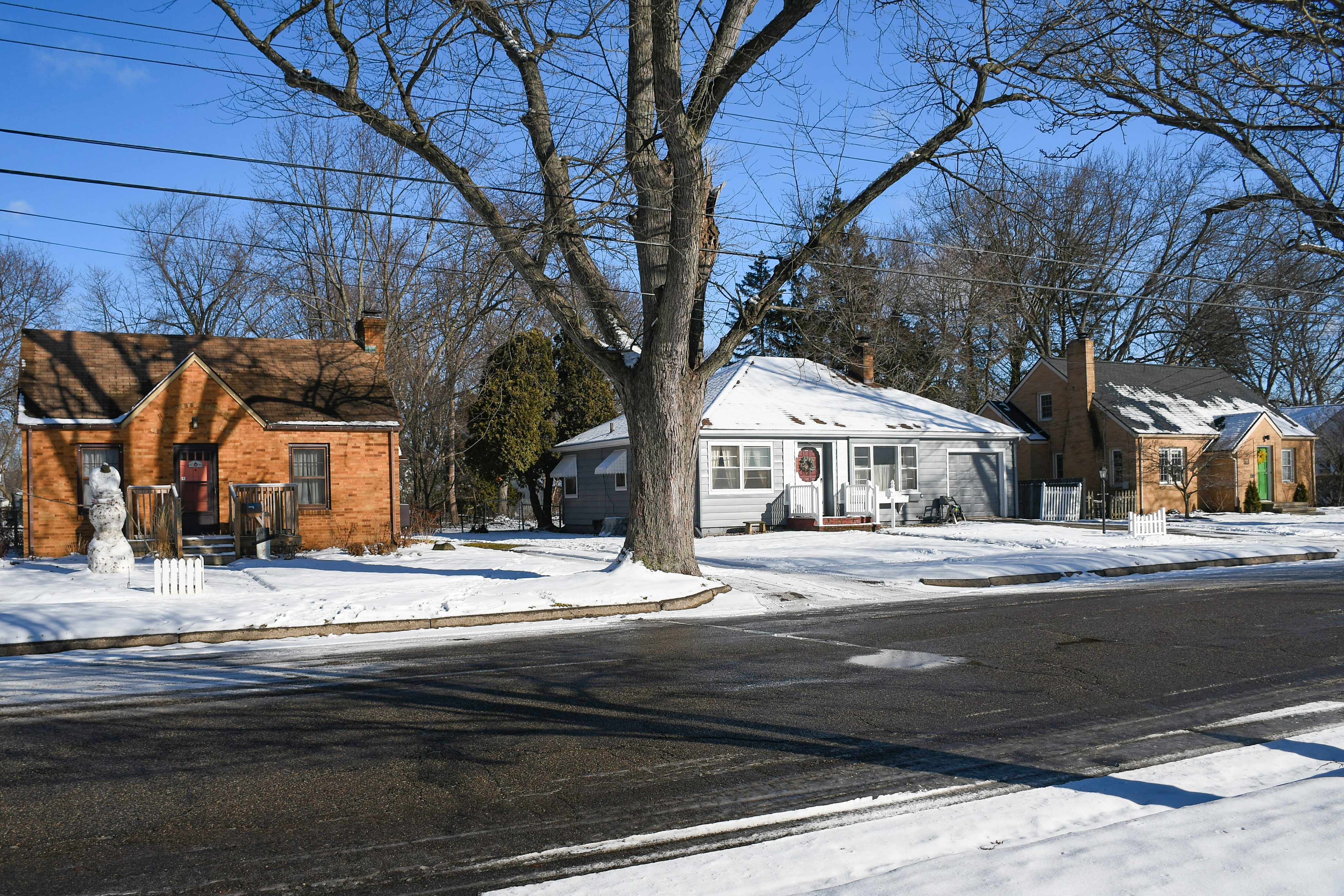 A grey house with a roof covered in snow and ice requiring cleaning and maintenance in the wintertime. 